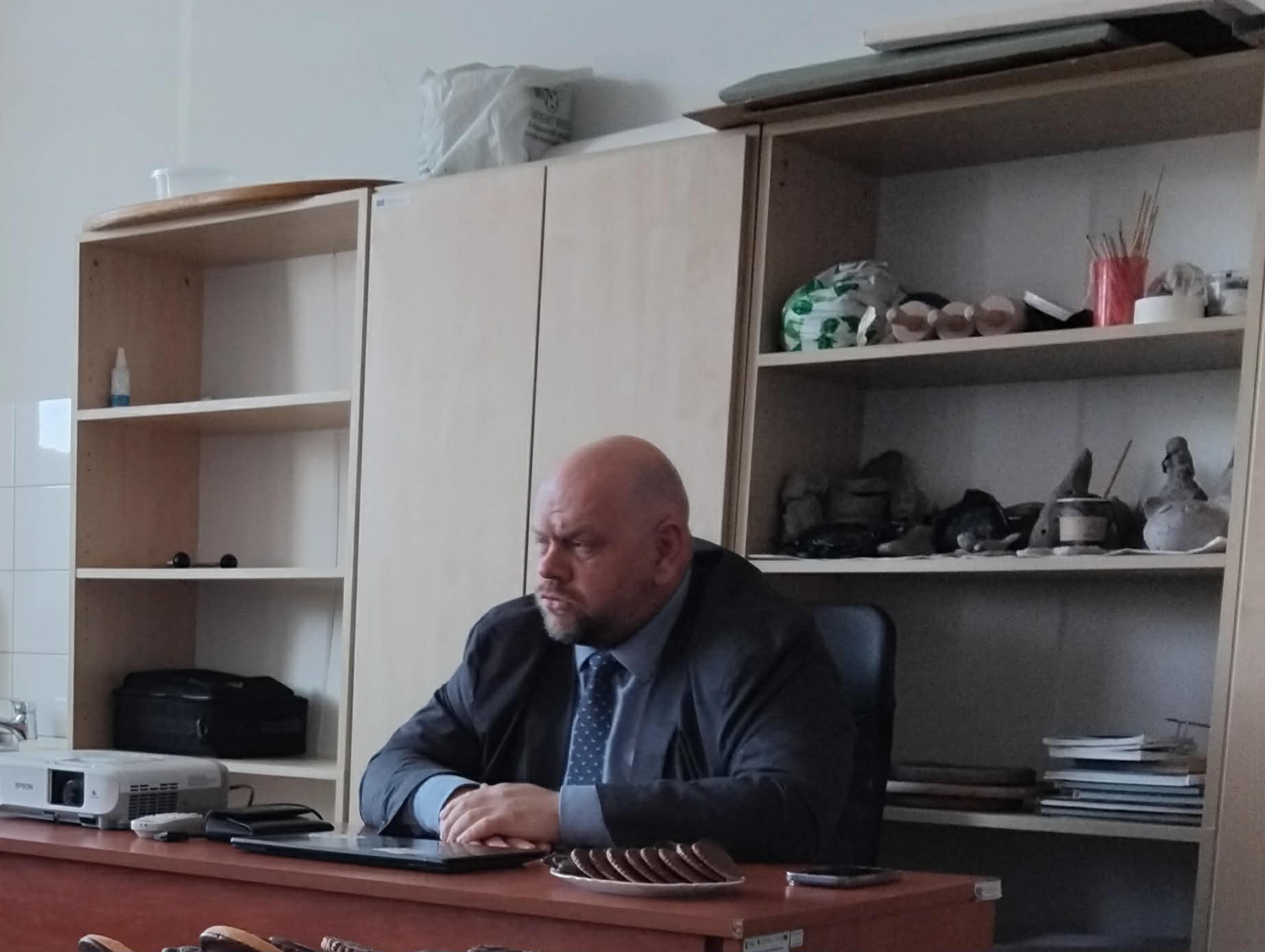 mężczyzna siedzacy za biurkie, w tle meble z półkami
